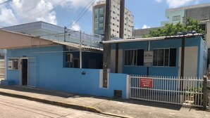 A small, single-story building with a blue exterior and a white fence. - Suíte Barros (Navegantes)
