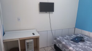 A bedroom with a bed, a TV mounted on the wall, a heater, and a small table with a remote control. - Suíte Barros (Navegantes)