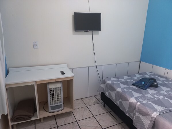 A bedroom with a bed, a TV mounted on the wall, a heater, and a small table with a remote control. - Suíte Barros (Navegantes)