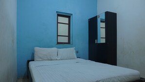 A small, single-bed room with a blue wall, a window, and a wardrobe.