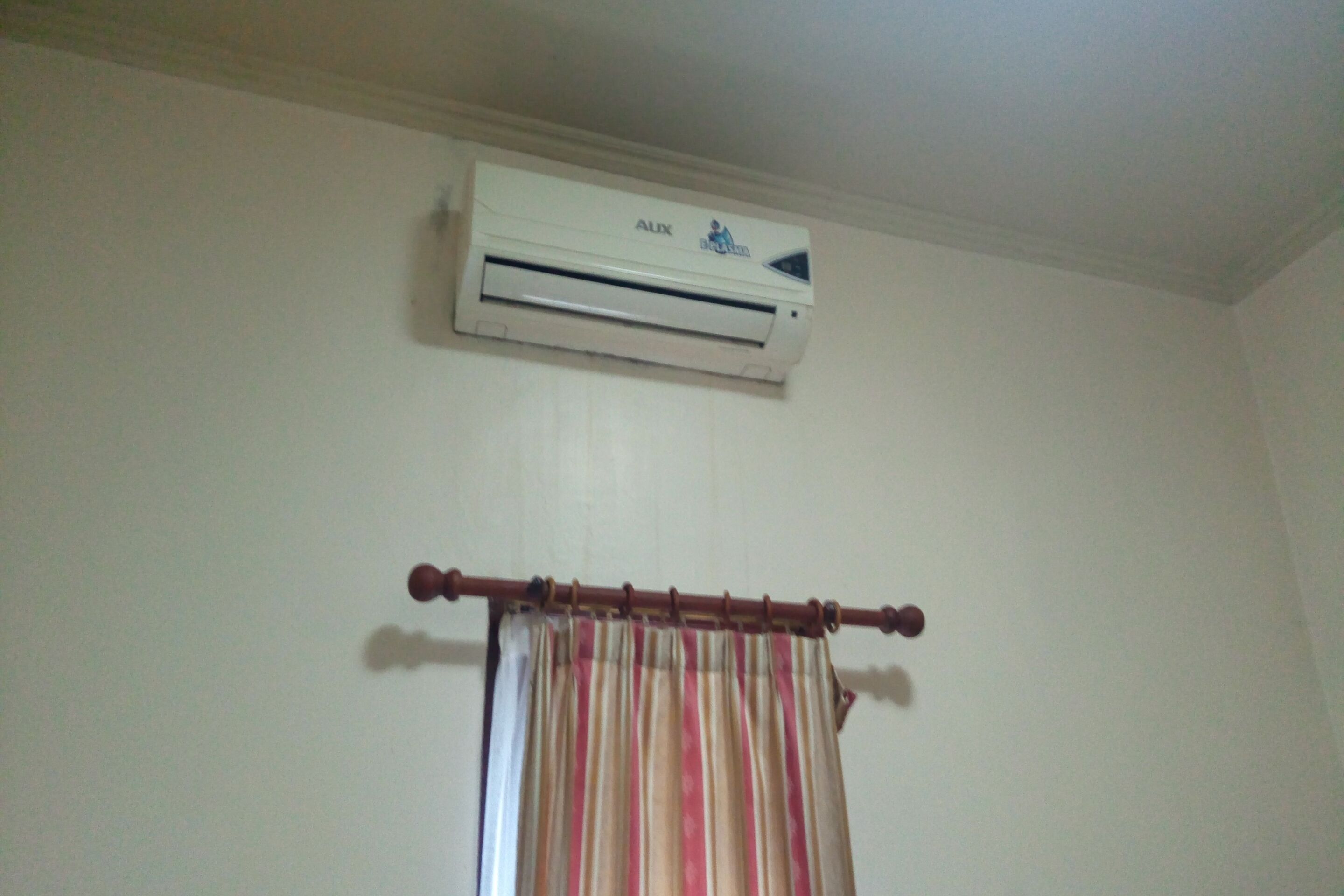Een kamer met een witte airconditioner die aan de muur bevestigd is en een gordijnroede met een gestreept gordijn.