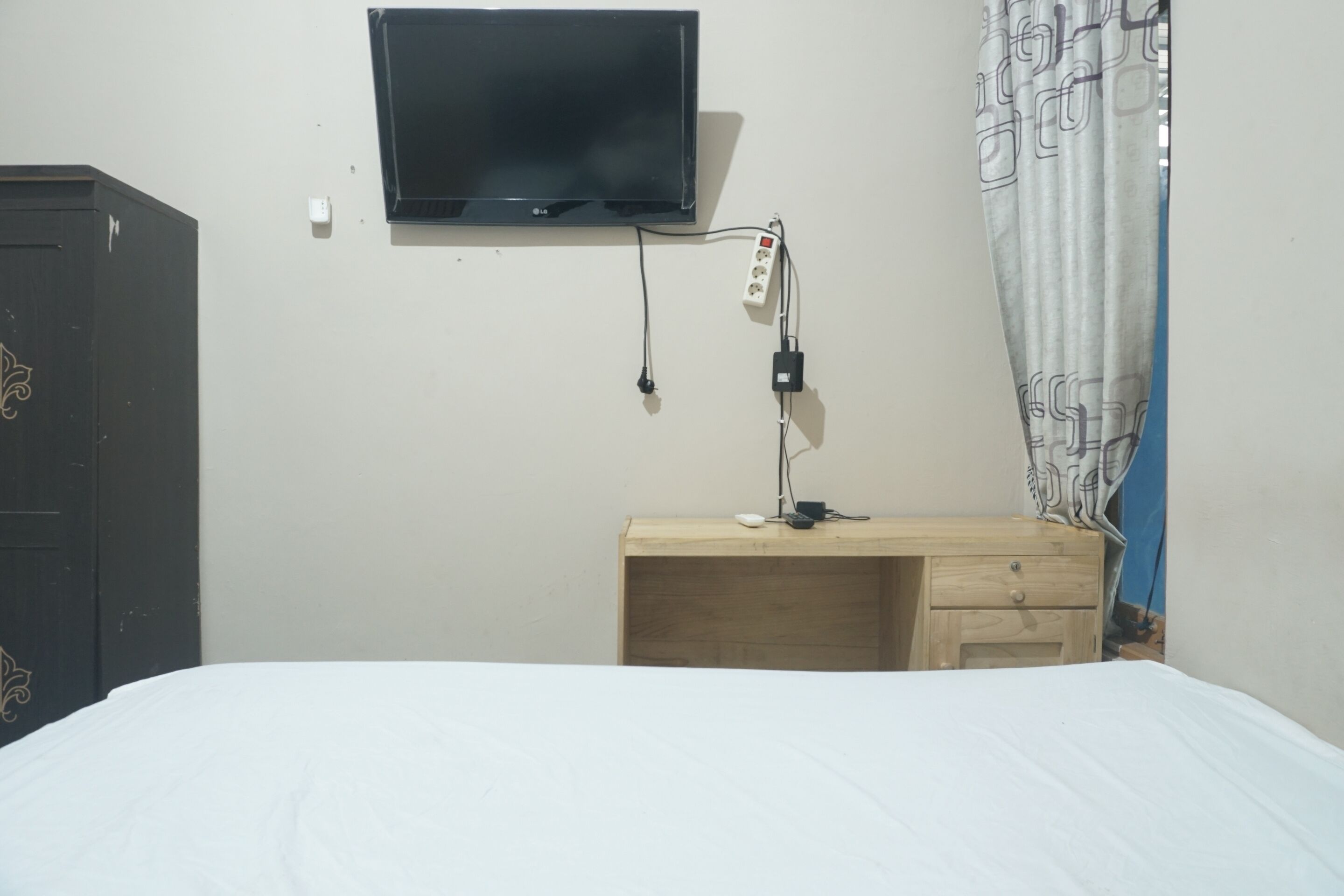 Une chambre à coucher comprenant un lit, un téléviseur fixé au mur, un bureau avec une lampe et une armoire.