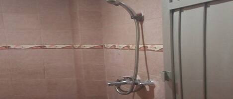 A shower area with a handheld showerhead and a wall-mounted faucet.