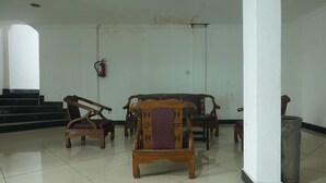 A room with a tiled floor, a wooden chair in the foreground, a wooden sofa, and a fire extinguisher on the wall.