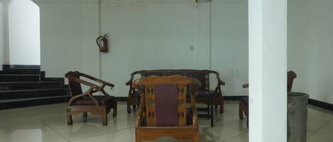 A room with a tiled floor, a wooden chair in the foreground, a wooden sofa, and a fire extinguisher on the wall.