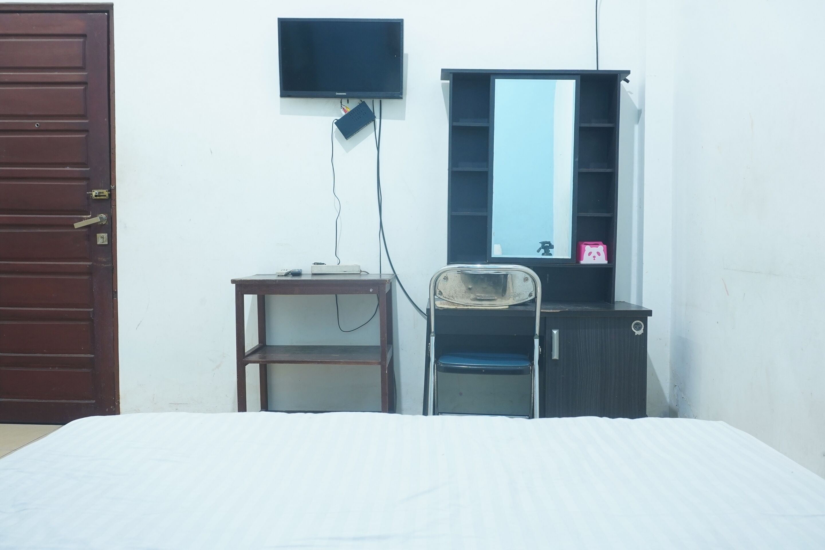 A bedroom with a bed, a desk, a chair, a wardrobe, a television, and a door.