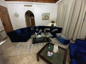 A living room with a blue sofa set, a glass coffee table, and a painting on the wall. - Au Temps Des Fleurs (Marrakech)