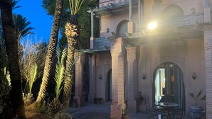 Un edificio tradicional con patio, palmeras y zona de comedor con mesas al aire libre.