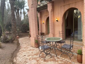 A patio with a round table and chairs, surrounded by brick pillars and arches, with potted plants and a view of the interior. - Au Temps Des Fleurs (Marrakech)