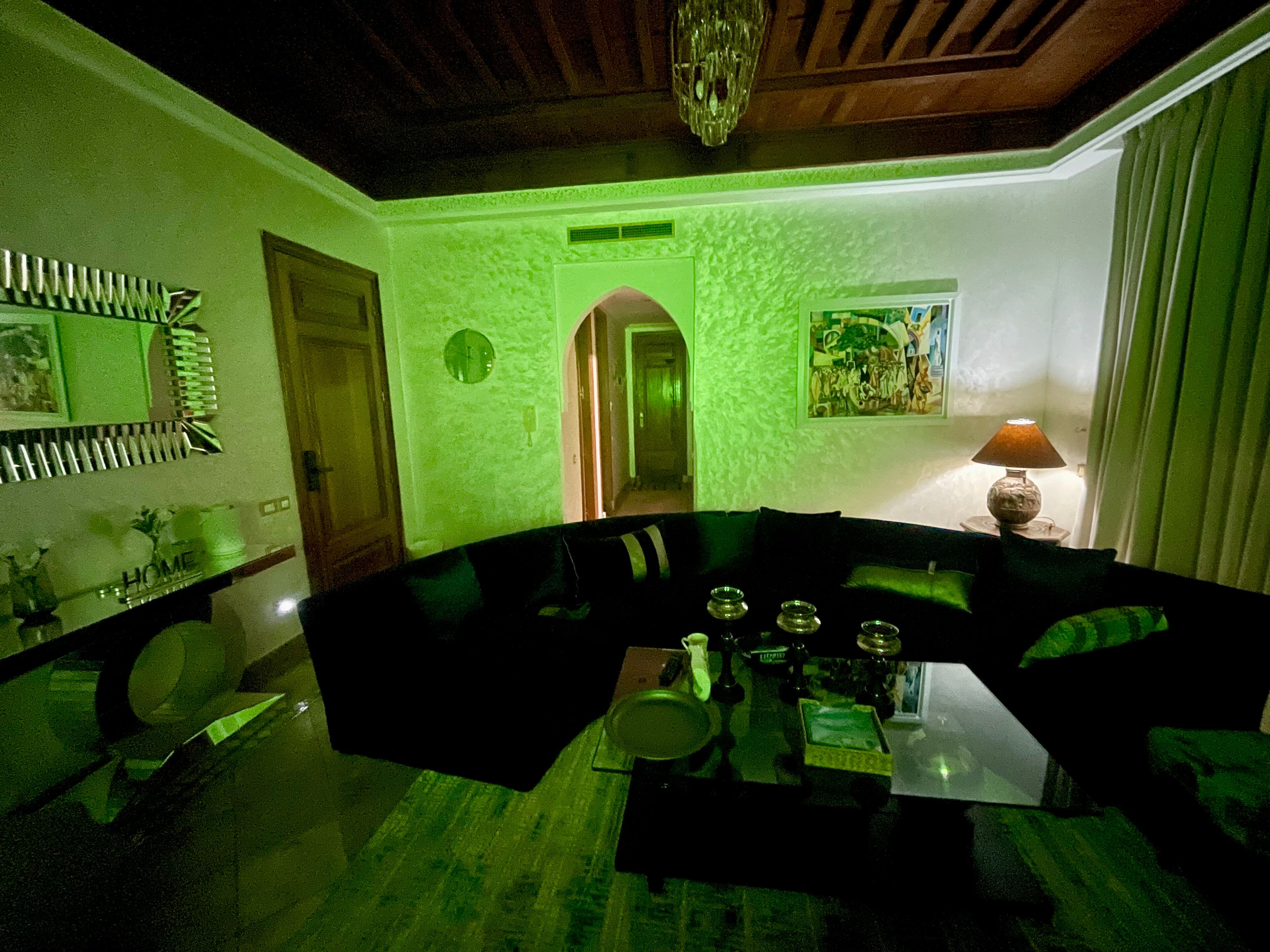 A room with a curved sofa, a dining table with plates and a lamp, a mirror, and a painting on the wall.