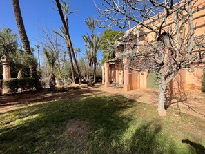 A courtyard with palm trees, a brick building, and a grassy area. - Au Temps Des Fleurs (Marrakech)