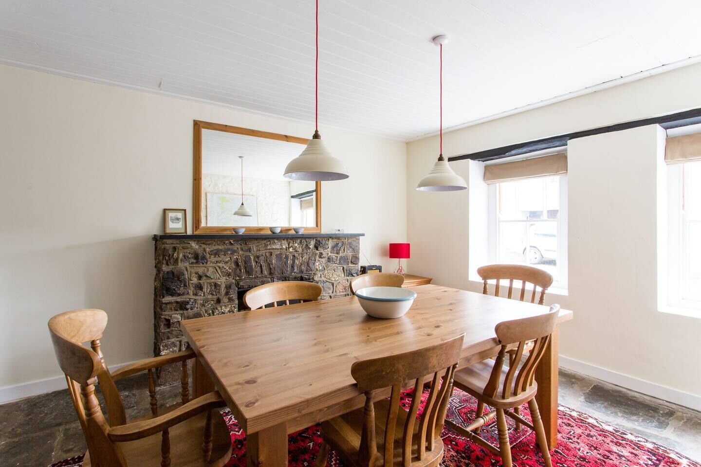 A dining area with a wooden table and chairs, a stone fireplace, and pendant lighting.
