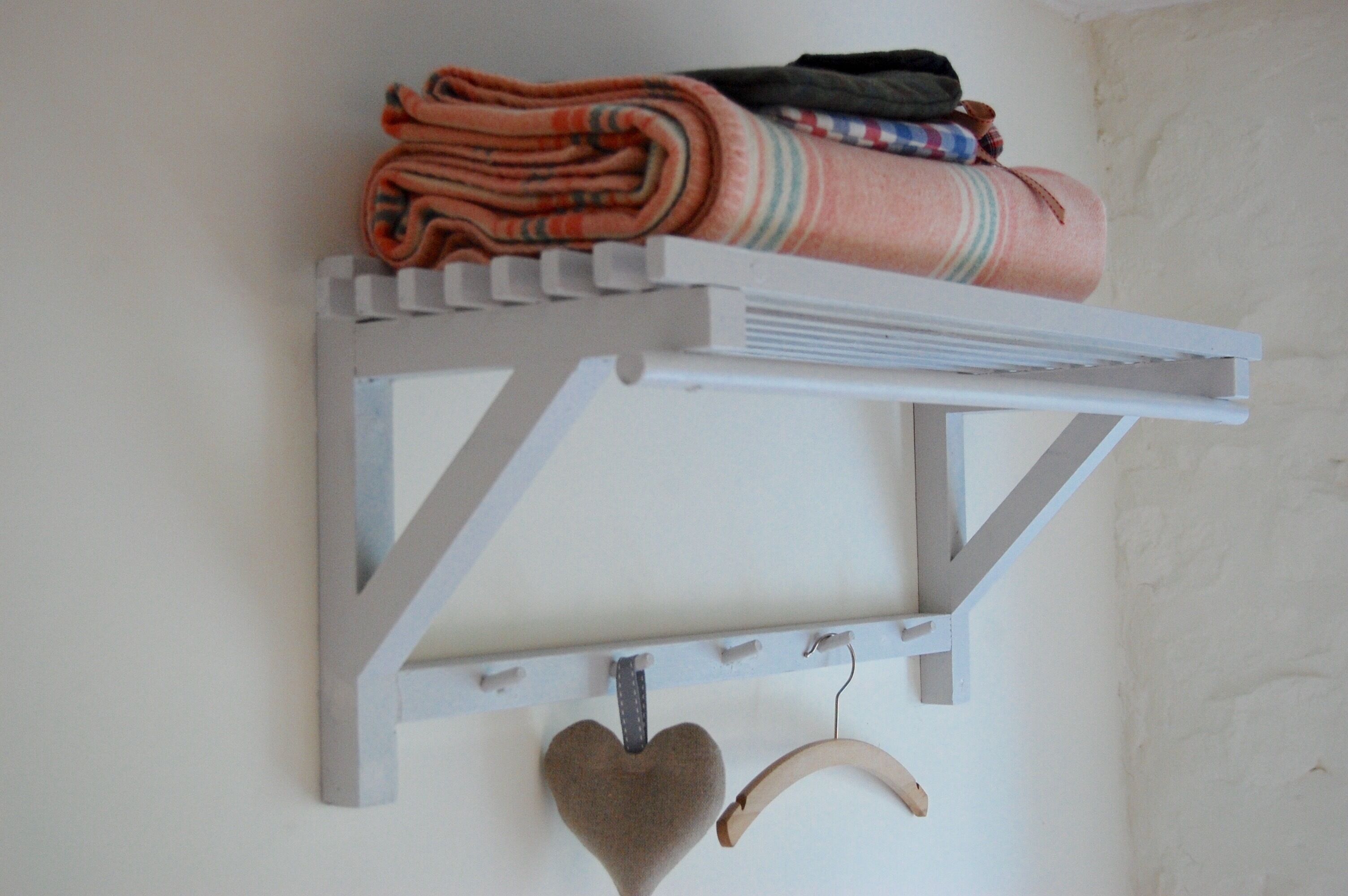 A white wall-mounted shelf with folded blankets and a heart-shaped decoration.