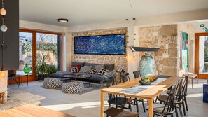 A modern living room with a stone wall, a large abstract painting, and a dining area with a wooden table and chairs.