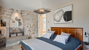 A bedroom with a stone wall, a bed with patterned pillows, a wooden headboard, and a hanging light fixture. - Villa Maxima Agri by Villas Guide (Porec)