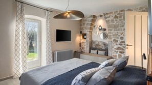 A bedroom with a bed, a stone wall, a mounted TV, and a window with curtains.