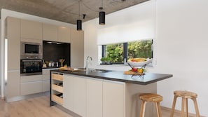 Una cocina moderna con una isla central, electrodomésticos de acero inoxidable y un ventanal con vistas al verdor.