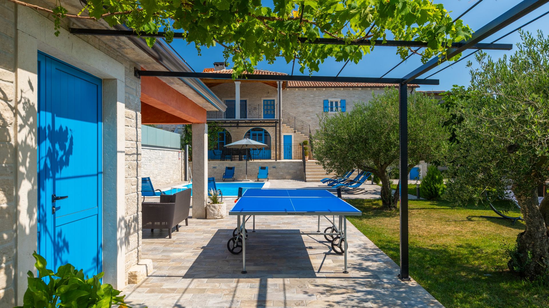 A pool area with a ping pong table, lounge chairs, and a blue door.