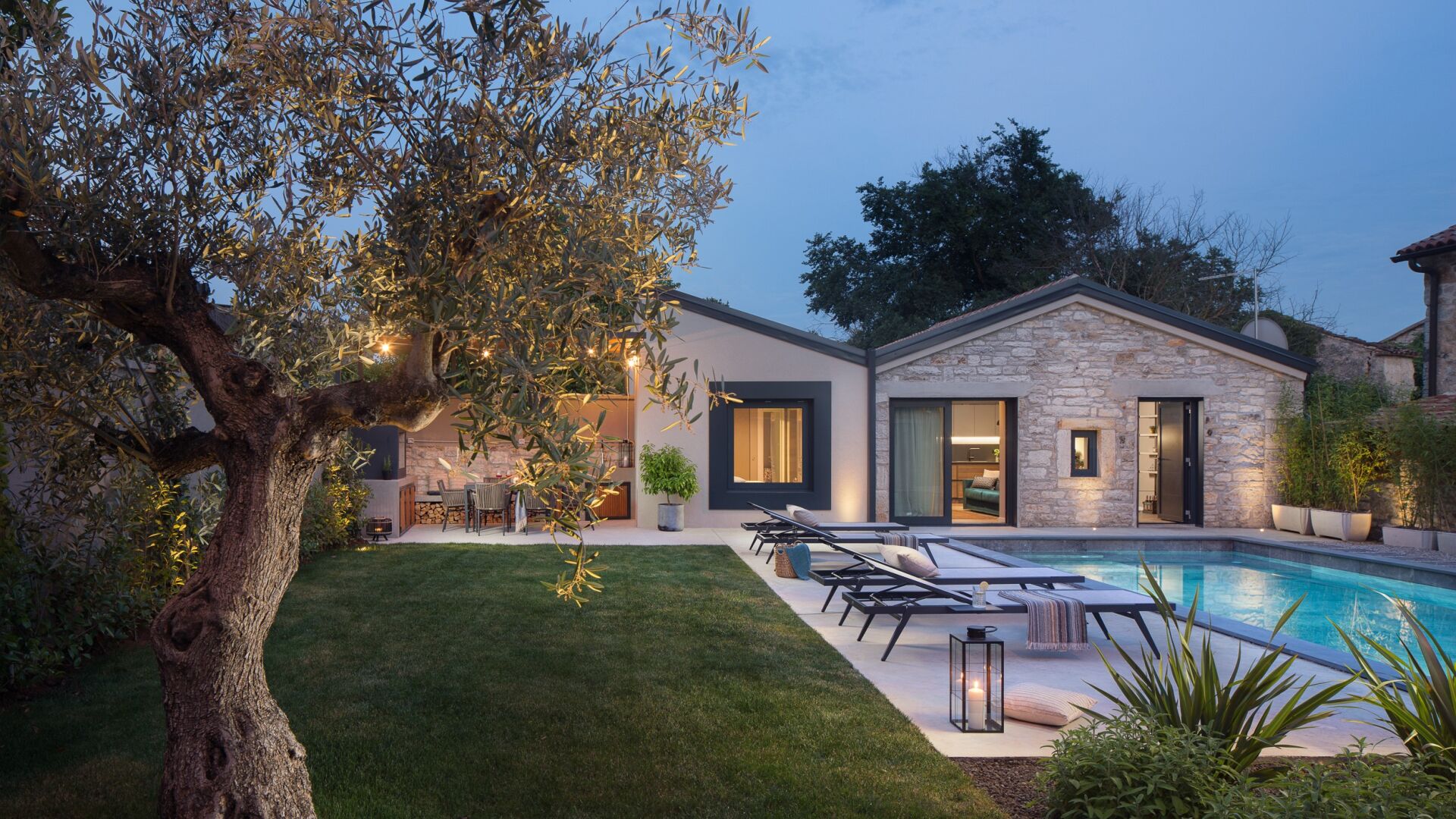 A modern house with a swimming pool, stone exterior, and a well-maintained lawn.