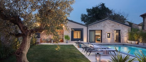 A modern house with a swimming pool, stone exterior, and a well-maintained lawn.