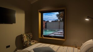 A bedroom with a large window overlooking a swimming pool, a flat-screen TV mounted on the wall, a patterned armchair, and a bedside table with a lamp. - Villa Bino&Marija by Villas Guide (Sveti Lovrec)