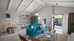A spacious living room with a teal sofa, a dining area with a wooden table, and a view of an outdoor swimming pool through large windows. - Villa Bino&Marija by Villas Guide (Sveti Lovrec)