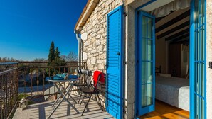 Een stenen gebouw met blauwe luiken, een balkon met een tafel en stoelen, en een bed dat van binnenuit zichtbaar is.