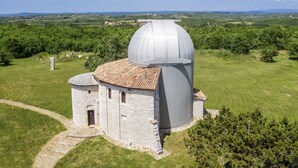 Een stenen observatorium met koepel en een kleiner, rond gebouw, omgeven door een grasveld en bomen.