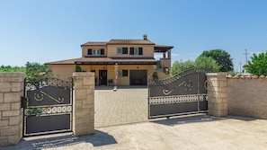 Une maison à deux étages, avec un toit en tuiles, un porche à l’avant et une allée menant à une porte grillagée.
