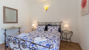 A neatly made bed with a floral bedspread, two bedside tables with lamps, a wall-mounted mirror, and a framed picture on the wall.
