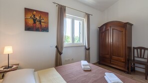 Une chambre à coucher comprenant un lit, une table de chevet, une lampe, une fenêtre avec des rideaux, une armoire en bois et une chaise.