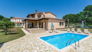 Une maison à deux étages avec une piscine, une terrasse en pierre et un espace salon extérieur.