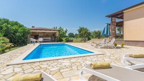 Une piscine avec des carreaux de pierre, des chaises longues et un espace patio couvert.
