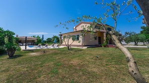 A two-story house with a swimming pool, a garden, and a tree in the foreground.