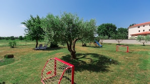 A grassy outdoor area with a playground, including a slide and swings, and a red goalpost.