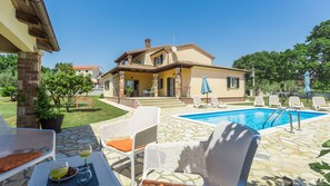 Une maison à deux étages avec une piscine, un espace salon extérieur et un jardin.