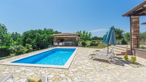 Une piscine revêtue de carrelage en pierre, une cuisine extérieure couverte et des chaises longues.