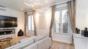 A modern living room with a large flat-screen TV, a sofa, a coffee table, and a decorative sculpture. - A Delightful 2-BR/2BA at Saint Michel - Notre Dame (Paris)