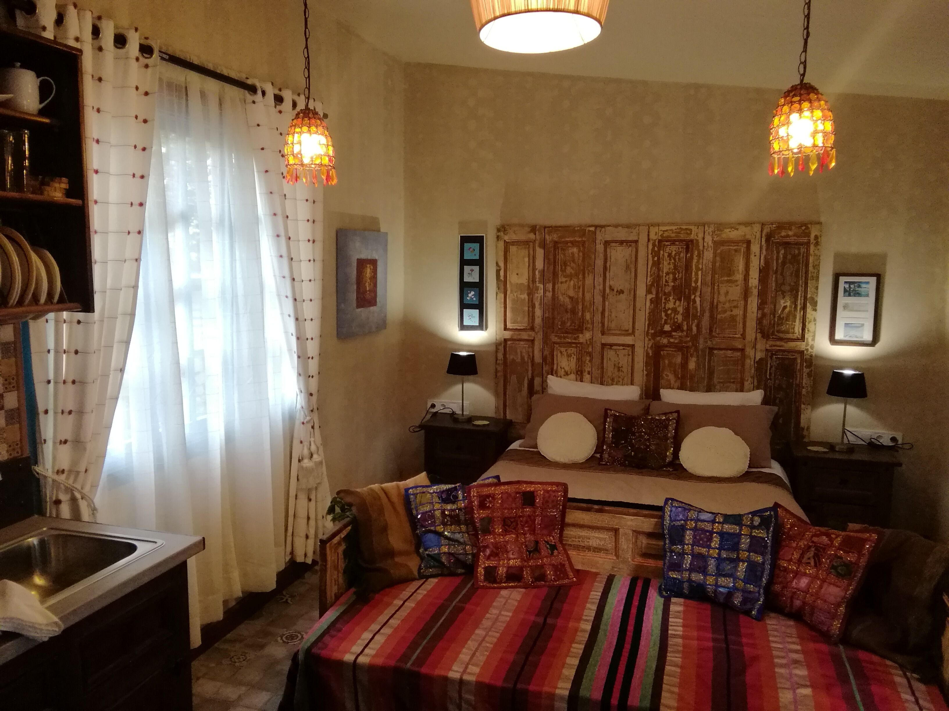 A bedroom with a large bed, two bedside tables with lamps, a wooden headboard, and a curtain with a pattern.