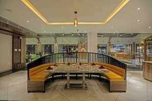 A modern indoor seating area with a curved bench and a central table, surrounded by glass walls and a ceiling with recessed lighting.