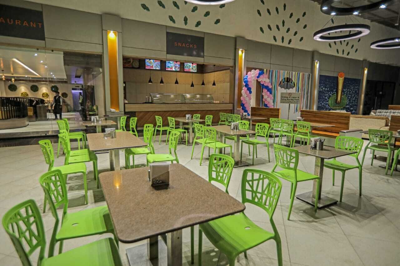Un restaurante con sillas y mesas verdes, una barra de aperitivos y un mostrador con una pantalla de menú.
