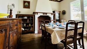 Une salle à manger avec une table en bois dressée pour quatre personnes, une cheminée et une bibliothèque remplie de livres et d’objets décoratifs.