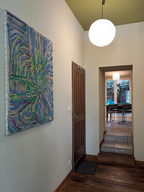 A hallway with a wooden door, a colorful abstract painting on the wall, and a staircase leading to a dining area. - Au Bord de la Rive (Lormont)