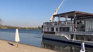 A boat with a covered deck and a person walking along the shore. - HMC Zahra Dahabyia (Armant)