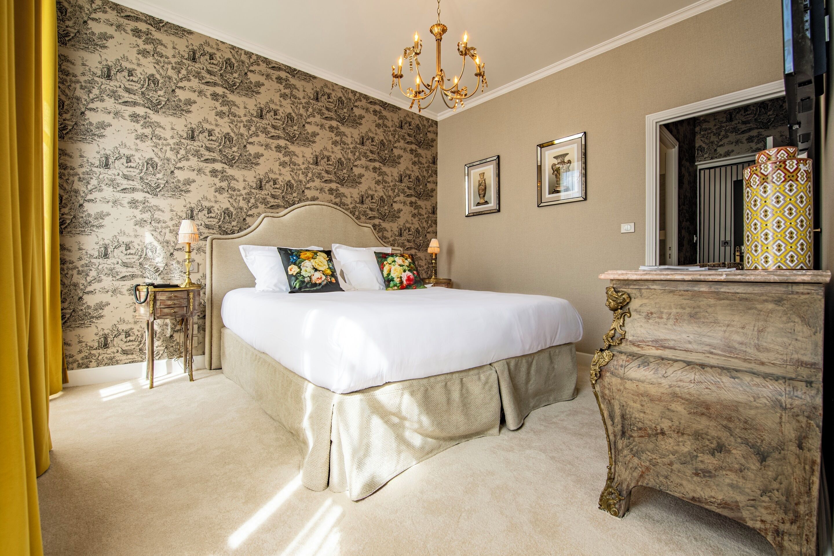 A bedroom with a large bed, a dresser, and a chandelier.