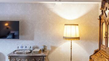 A room with a high ceiling, a wooden dresser, a floor lamp, and a television on the wall.