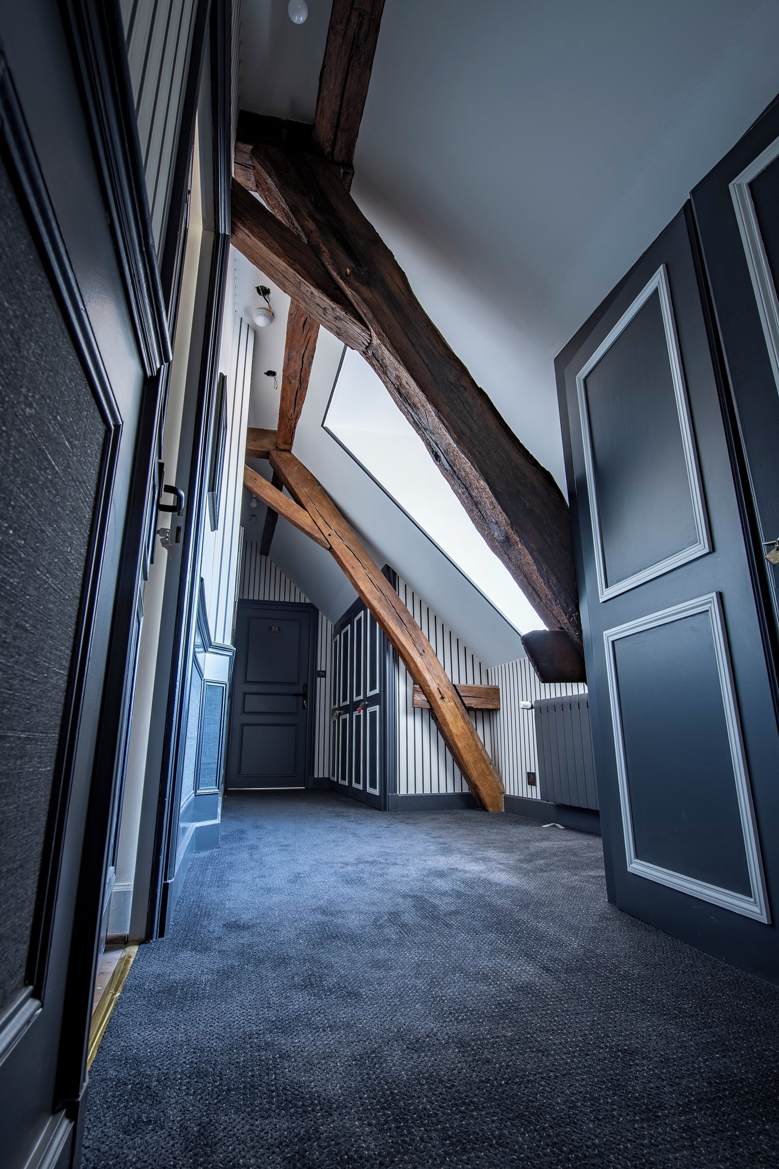 A hallway with a sloped ceiling, exposed wooden beams, and a carpeted floor.