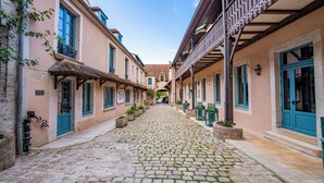 A cobblestone street flanked by buildings with blue doors and windows, a covered walkway, and outdoor seating areas.