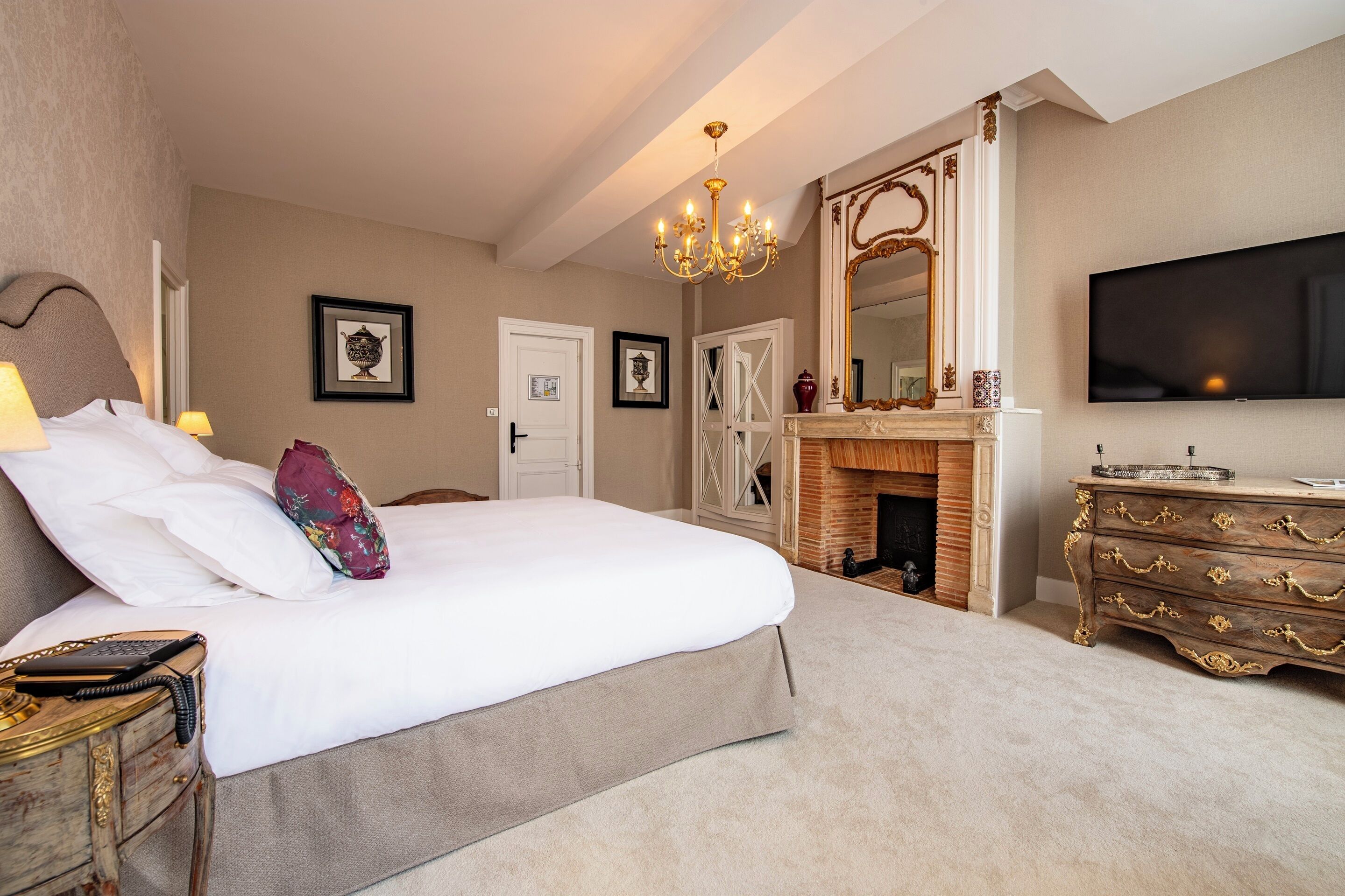 Een hotelkamer met een groot bed, een houten dressoir, een televisie en een open haard.