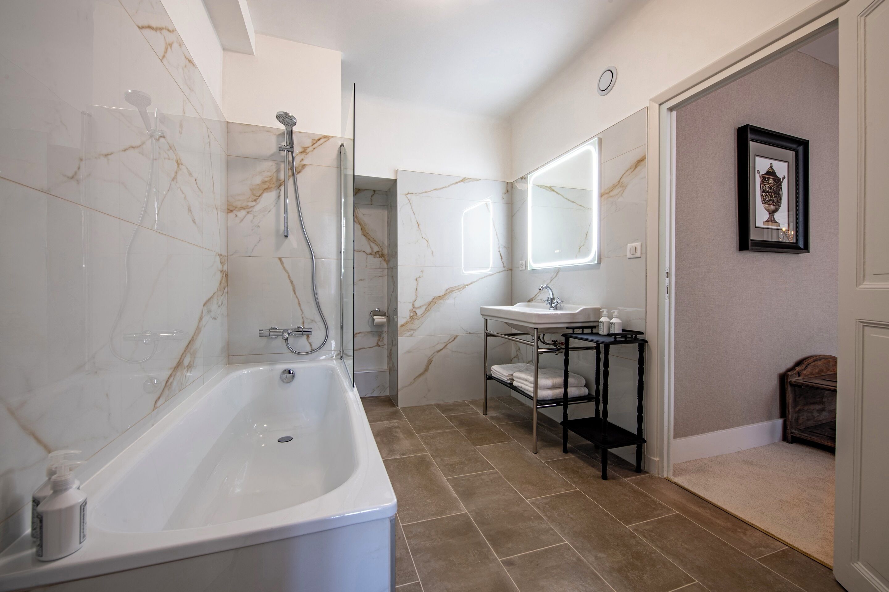 A modern bathroom with a marble shower, a standalone bathtub, a vanity with a mirror, and a small wooden cabinet.